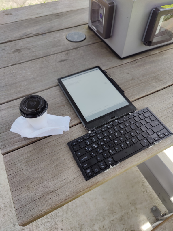 Photograph of a tablet with a draft of this post and a bluetooth  keyboard with a cup of coffee on a picnic table.